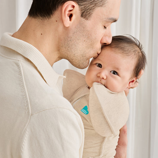 Man holding a baby in a beige wrap against a white background