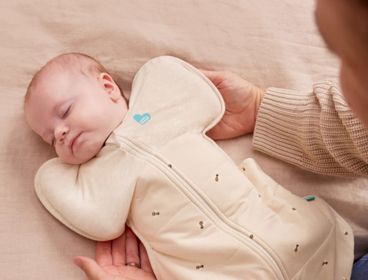 Baby sleeping in a beige baby swaddle 
with a heart tag, held by an adult.